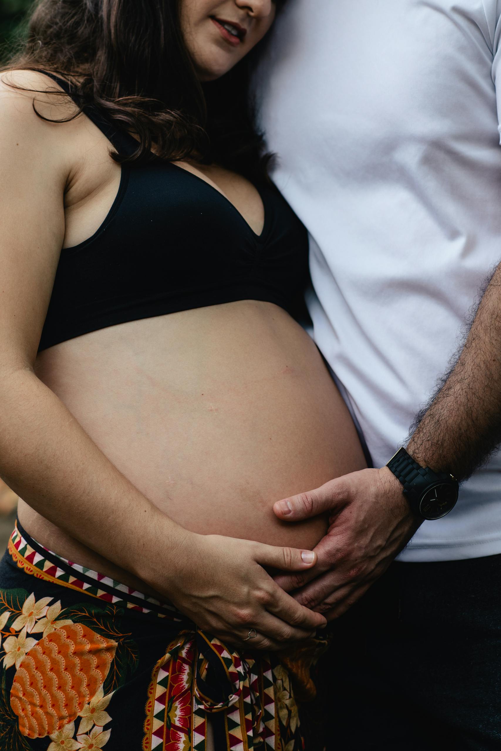 Close-up of an expecting couple embracing, highlighting the woman's pregnant belly and shared parental love.